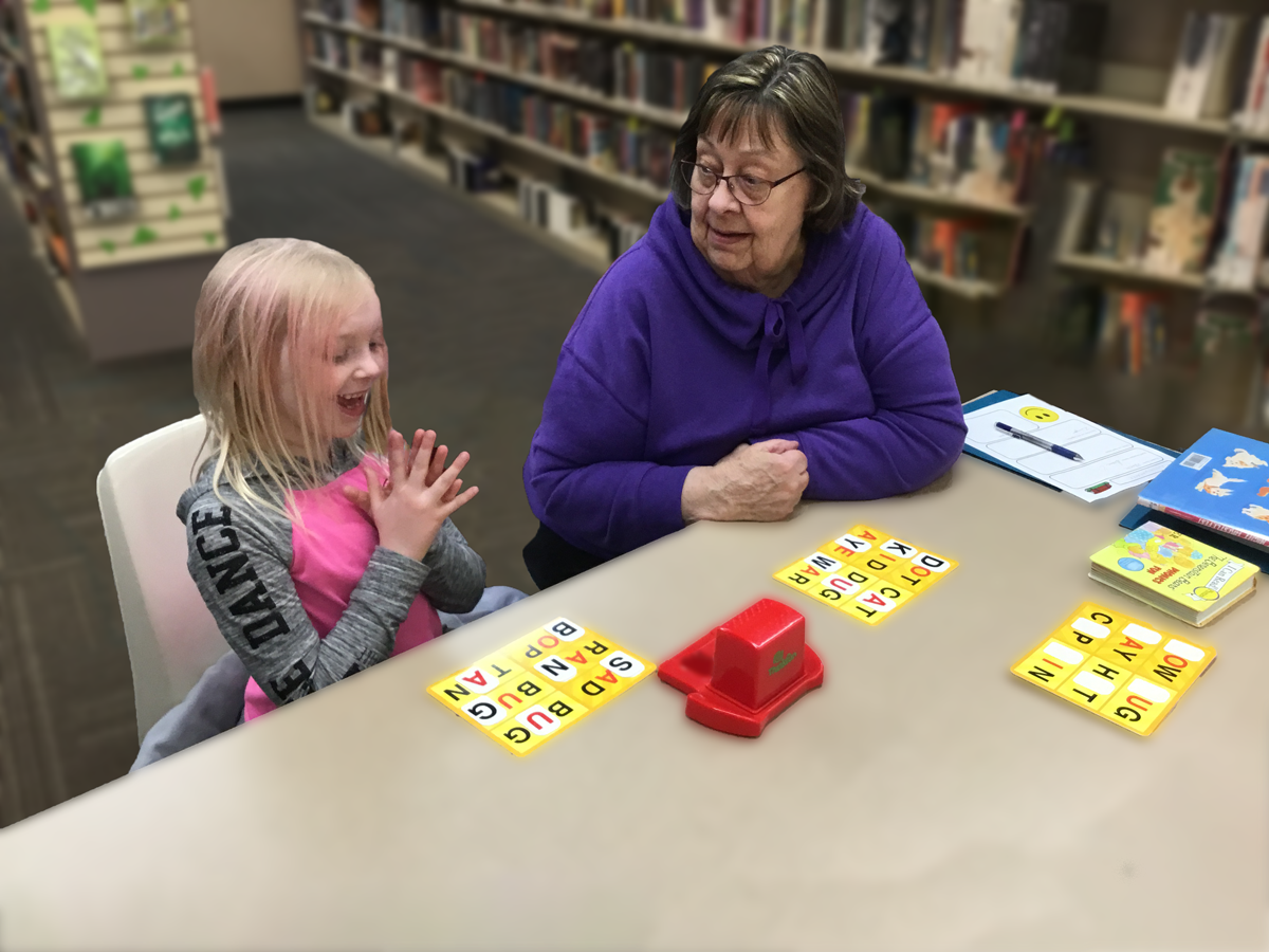 reading-bridge-girl and adult volunteer playing game at table