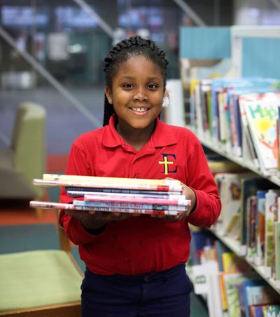 Young girl smiling with a stack of books in the library