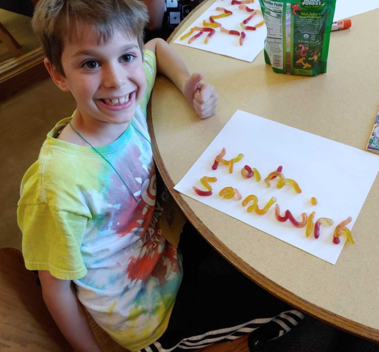 young boy with thumbs up has spelled his name in gummy worms